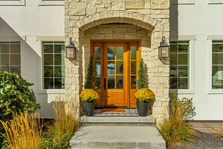 Entryway featuring a wood-panel door with glass inserts, stone archway, two wall-mounted lanterns, and grid-pattern windows