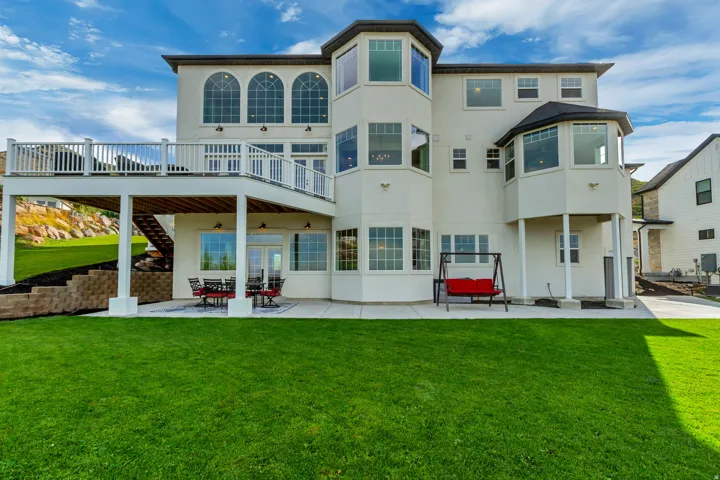 Expansive backyard featuring a manicured lawn, a concrete patio, a raised deck with white railings, and a retaining wall