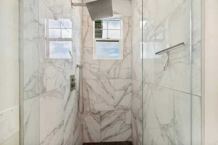 Walk-in shower with full-height marble-look tile, rain shower head, handheld shower, and glass enclosure
