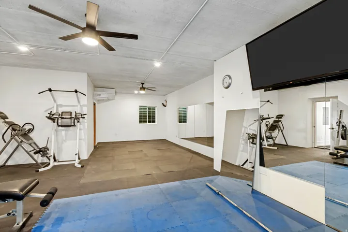 Spacious room featuring ceiling fans, wall-mounted television, full-length mirrors, and durable flooring