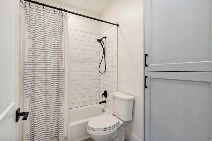 Tub and shower combination with white subway tile surround, matte black fixtures, and built-in white cabinetry with black pulls
