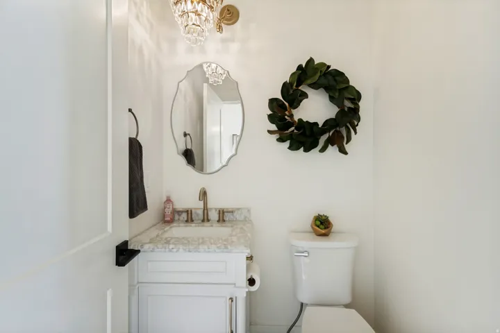 White vanity with a marble-finish countertop, brass-finish faucet, and an ornate wall-mounted light fixture