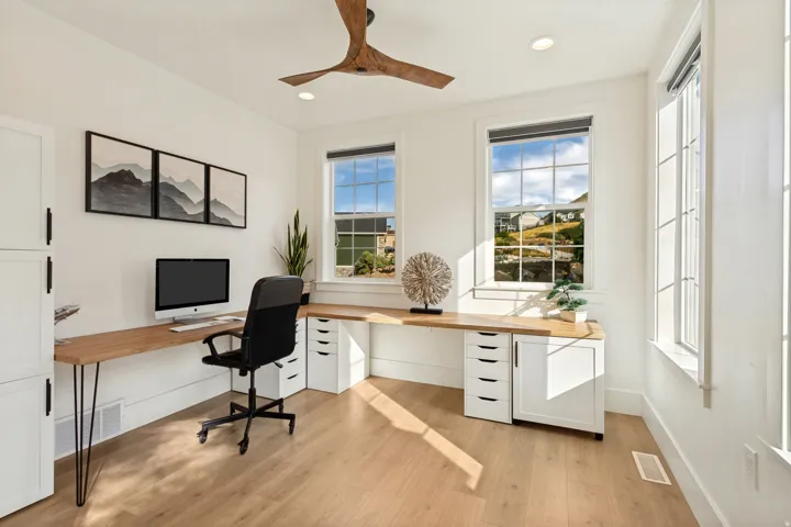 Light wood-finish flooring, built-in desk with white cabinetry, wood ceiling fan, recessed lighting, and multiple windows