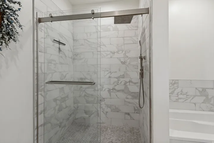Glass-enclosed shower with subway tile surround, rain shower head, hand-held shower fixture, and herringbone tile flooring