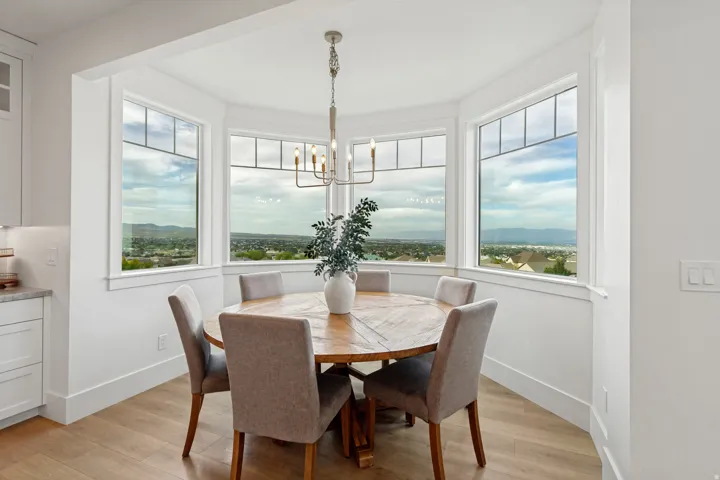 Bay window with multiple large panes, wood-finish flooring, white cabinetry, and a contemporary chandelier