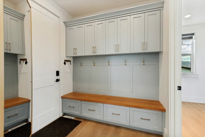 Custom built-in cabinetry with light-toned finish, wood-finish bench, and integrated coat hooks