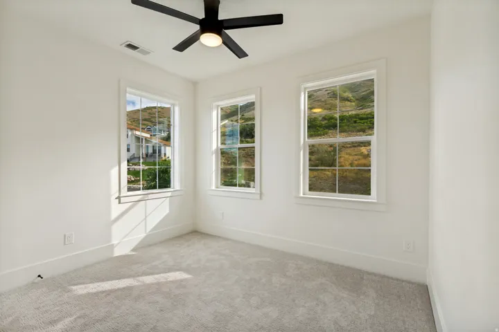Light-filled room featuring three single-hung windows, a ceiling fan with integrated lighting, and wall-to-wall carpeting