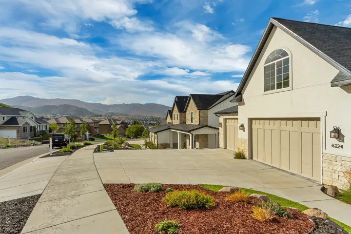 Stucco exterior with stone accents, arched window, attached two-car garage, and established landscaping