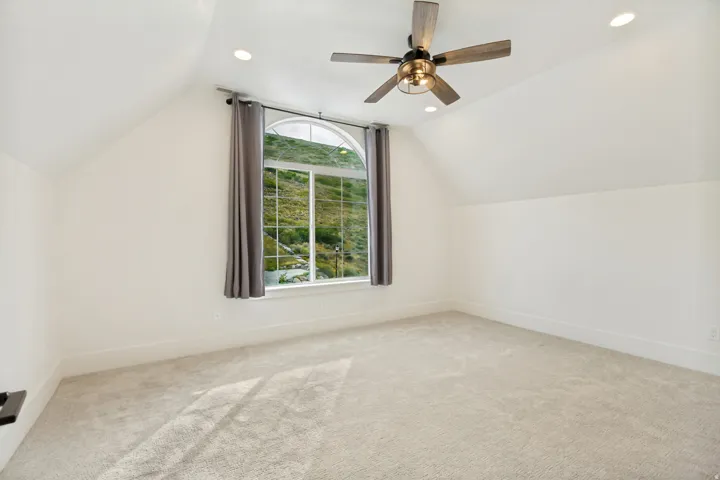 Arched window, vaulted ceiling, recessed lighting, ceiling fan, and light-toned carpeting