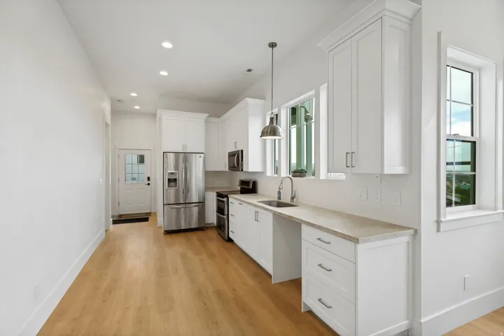 White shaker cabinetry, stainless steel appliances, wood-finish flooring, recessed lighting, and a pendant light fixture