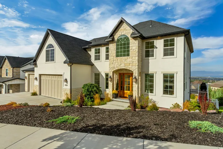 Stucco exterior with stone accents, a multi-car garage, an arched entryway, and mature landscaping