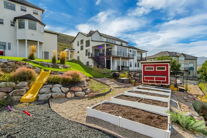 Expansive terraced backyard featuring multiple raised garden beds, a red storage shed, and a children's slide