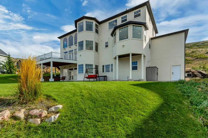 Multi-story stucco exterior with multiple bay windows, an elevated deck with white railings, and a covered patio below