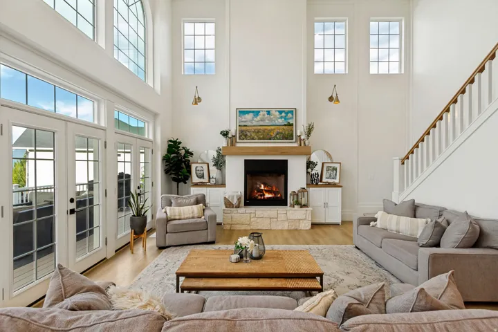 High ceilings featuring multiple windows, a stone-clad fireplace with a wood-finish mantel, and light wood-finish flooring