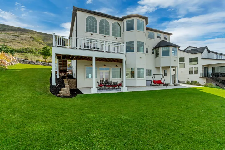 Expansive lawn with a two-story exterior, upper-level deck, lower-level patio, and multiple bay windows