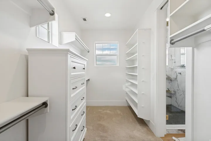 Spacious walk-in closet featuring extensive built-in shelving, hanging rods, an integrated dresser, and a window for natural light