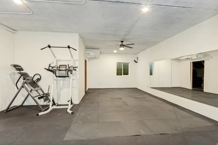 Spacious room featuring dark tile flooring, a ceiling fan, window with horizontal blinds, and a built-in wall mirror