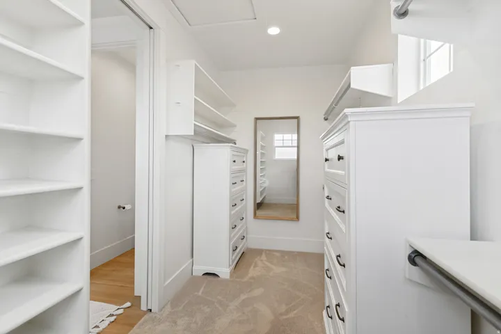 Built-in shelving, white cabinetry, carpeted flooring, recessed lighting, and a full-length mirror