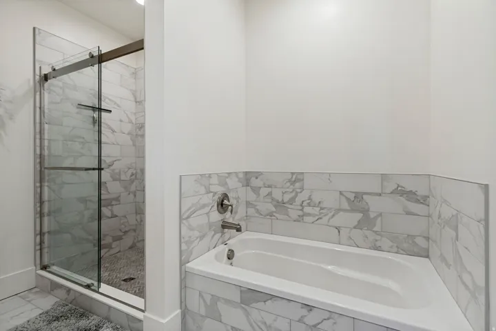 Built-in soaking tub with surround tile, glass-enclosed shower, wall-mounted shower faucet with handheld sprayer, and tiled shower walls