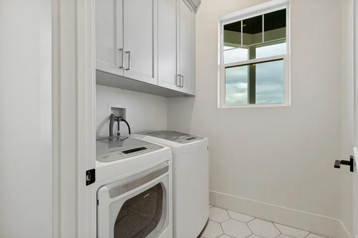 White shaker-style cabinetry with silver-tone hardware, a single-pane window, and white hexagonal floor tiles