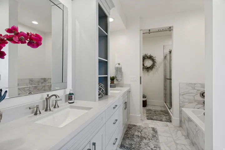 Dual sink vanity with white countertop, built-in shelving, marble-look tile flooring, and a shower enclosure with a sliding barn door
