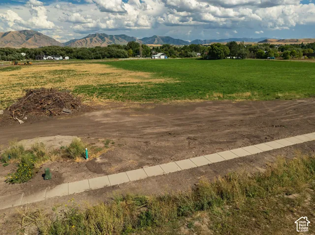 Expansive land parcel featuring a concrete pathway, a verdant green field, and distant mountains