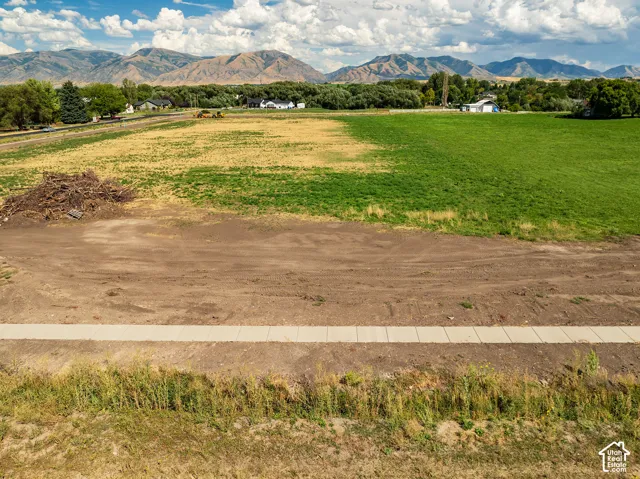 Expansive land parcel featuring a newly installed sidewalk, surrounded by open fields, and framed by distant mountains