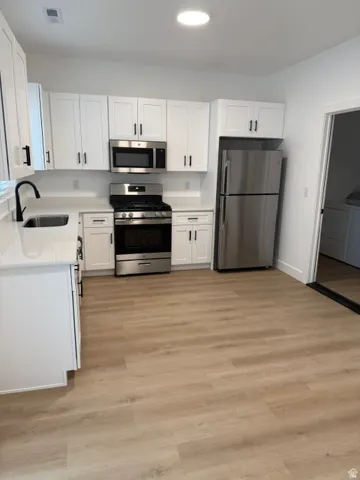 White shaker cabinetry, stainless steel appliances, wood-finish flooring, recessed lighting, and light-toned countertops