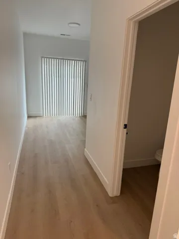 Wood-finish flooring throughout, bright white walls, recessed ceiling lighting, and vertical blinds on the sliding glass door
