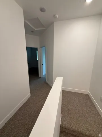 Carpeted hallway with white walls, recessed lighting, and a square ceiling access panel