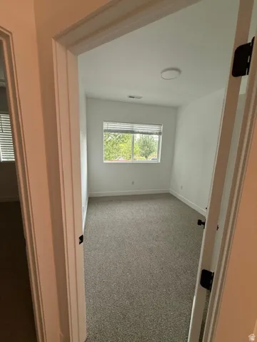 Neutral-toned carpet flooring, white walls, and a window with blinds provide a bright interior