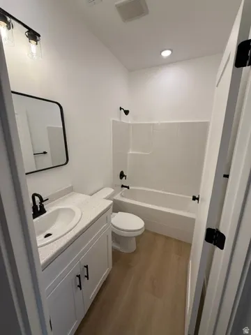 Modern bathroom featuring a white vanity with black hardware, a speckled countertop, black fixtures, and wood-finish flooring
