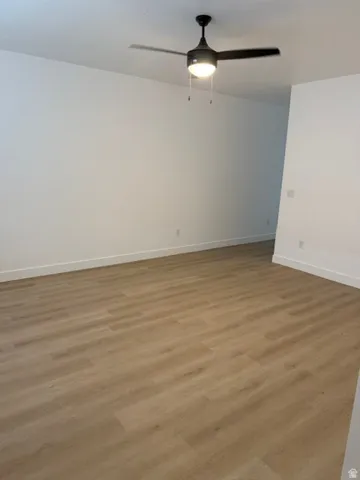 Wood-finish flooring with crisp white walls and a ceiling fan with integrated lighting
