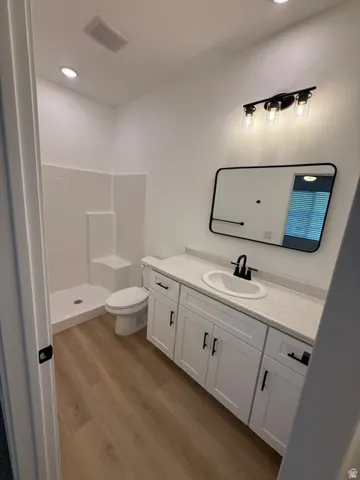 Wood-finish flooring, white vanity with black hardware, white countertop, rectangular mirror, and a black-finish vanity light