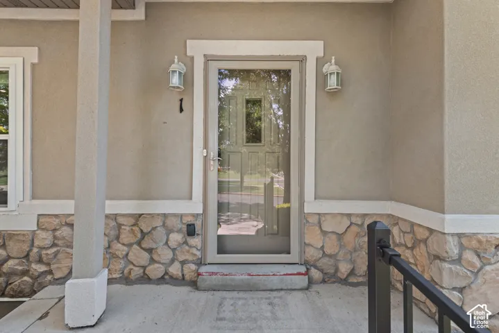 Stucco exterior with stone veneer accents, concrete porch, decorative outdoor lighting, and a storm door