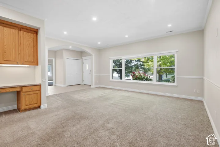 Recessed lighting, arched doorway, built-in desk with overhead cabinetry, paneled accent wall, and large picture windows