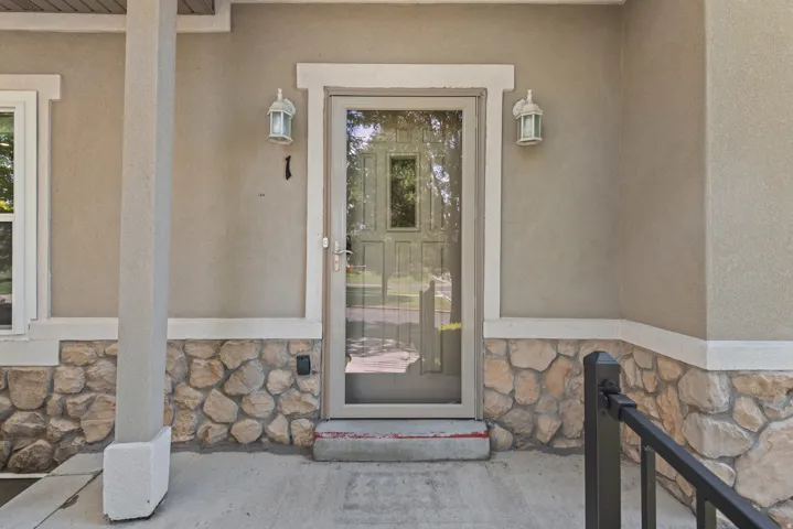 Stucco exterior with stone veneer accents, concrete porch, decorative outdoor lighting, and a storm door