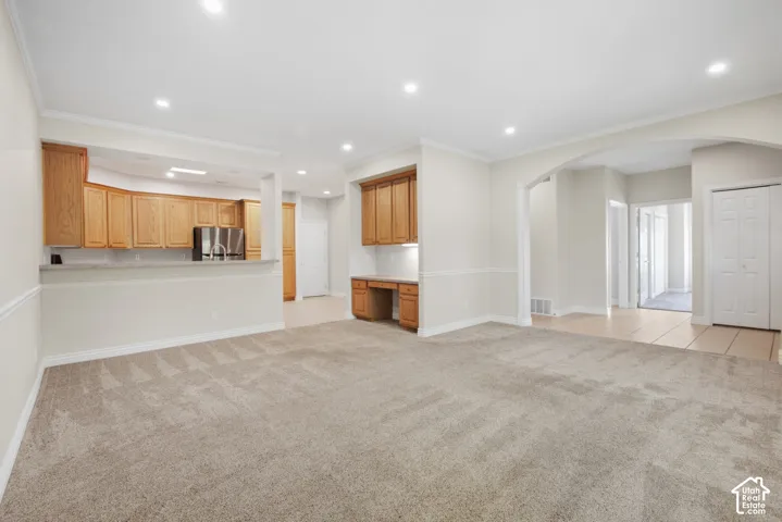 Recessed lighting illuminates the carpeted living area with chair rail molding, featuring an arched entryway and a built-in desk with overhead cabinetry