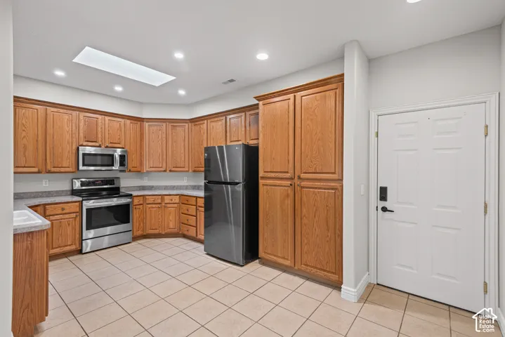 U-shaped kitchen with wood cabinetry, stainless steel appliances, and a skylight