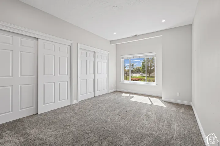 Recessed lighting, light gray wall finish, window with white trim, gray carpet, and white paneled closet doors