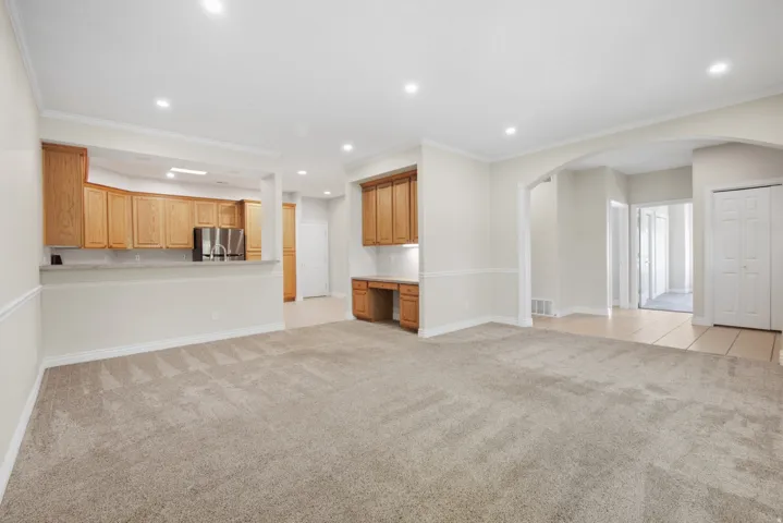 Recessed lighting illuminates the carpeted living area with chair rail molding, featuring an arched entryway and a built-in desk with overhead cabinetry