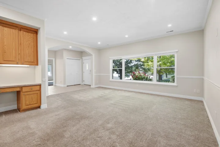 Recessed lighting, arched doorway, built-in desk with overhead cabinetry, paneled accent wall, and large picture windows