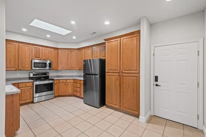 U-shaped kitchen with wood cabinetry, stainless steel appliances, and a skylight