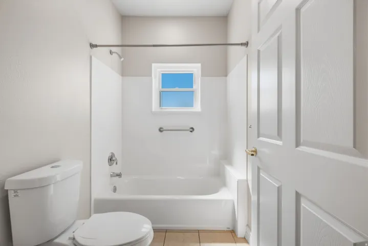 Bathroom featuring a white bathtub, ceramic tile flooring, a window, and a paneled door