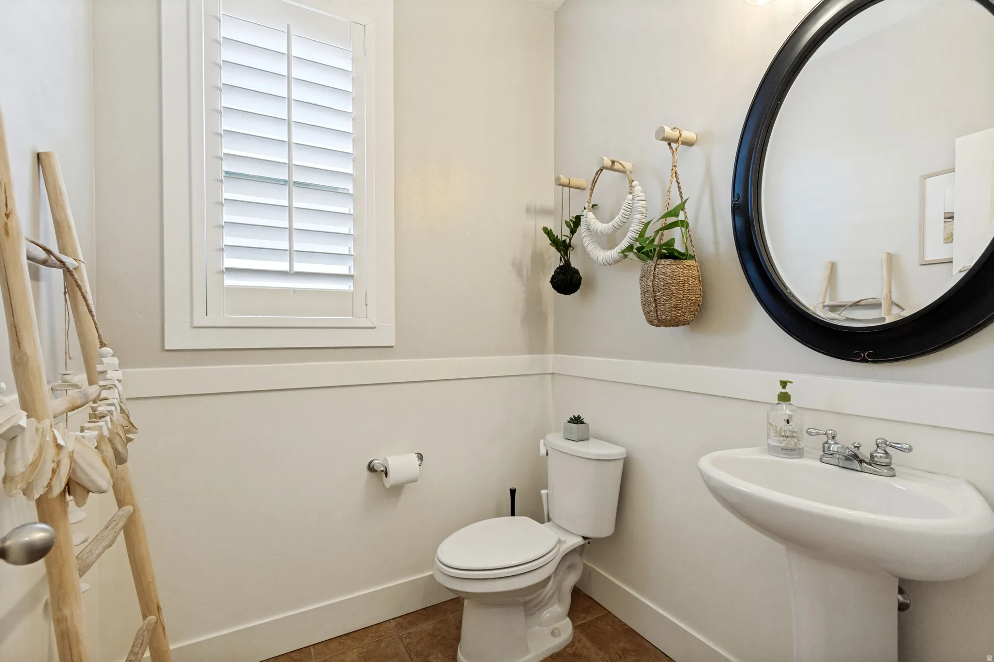 White plantation shutters, pedestal sink, wall-mounted oval mirror, toilet, and wood-finish flooring