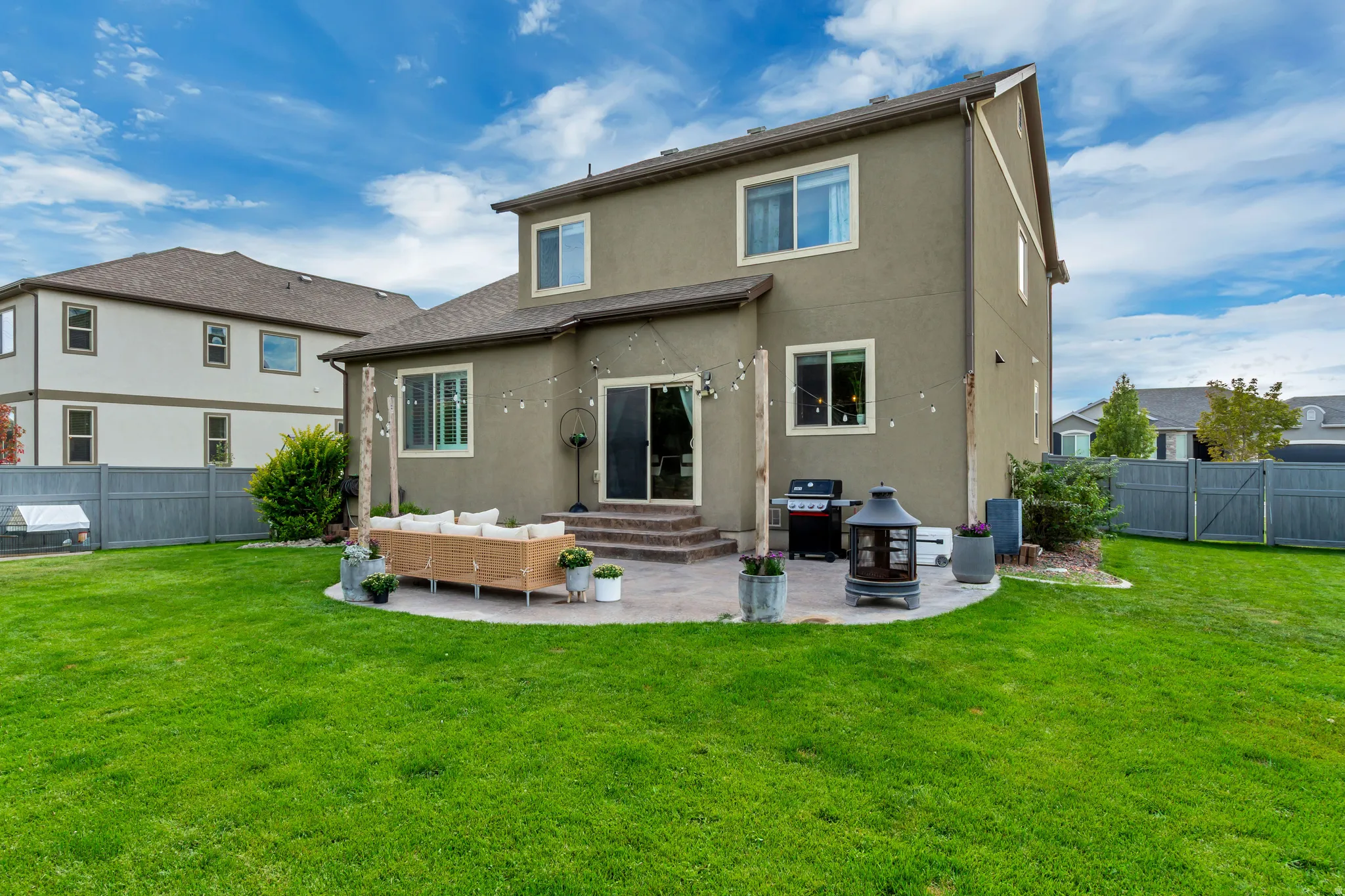 Expansive backyard featuring a large green lawn, a multi-level paver patio, stucco exterior, and a privacy fence