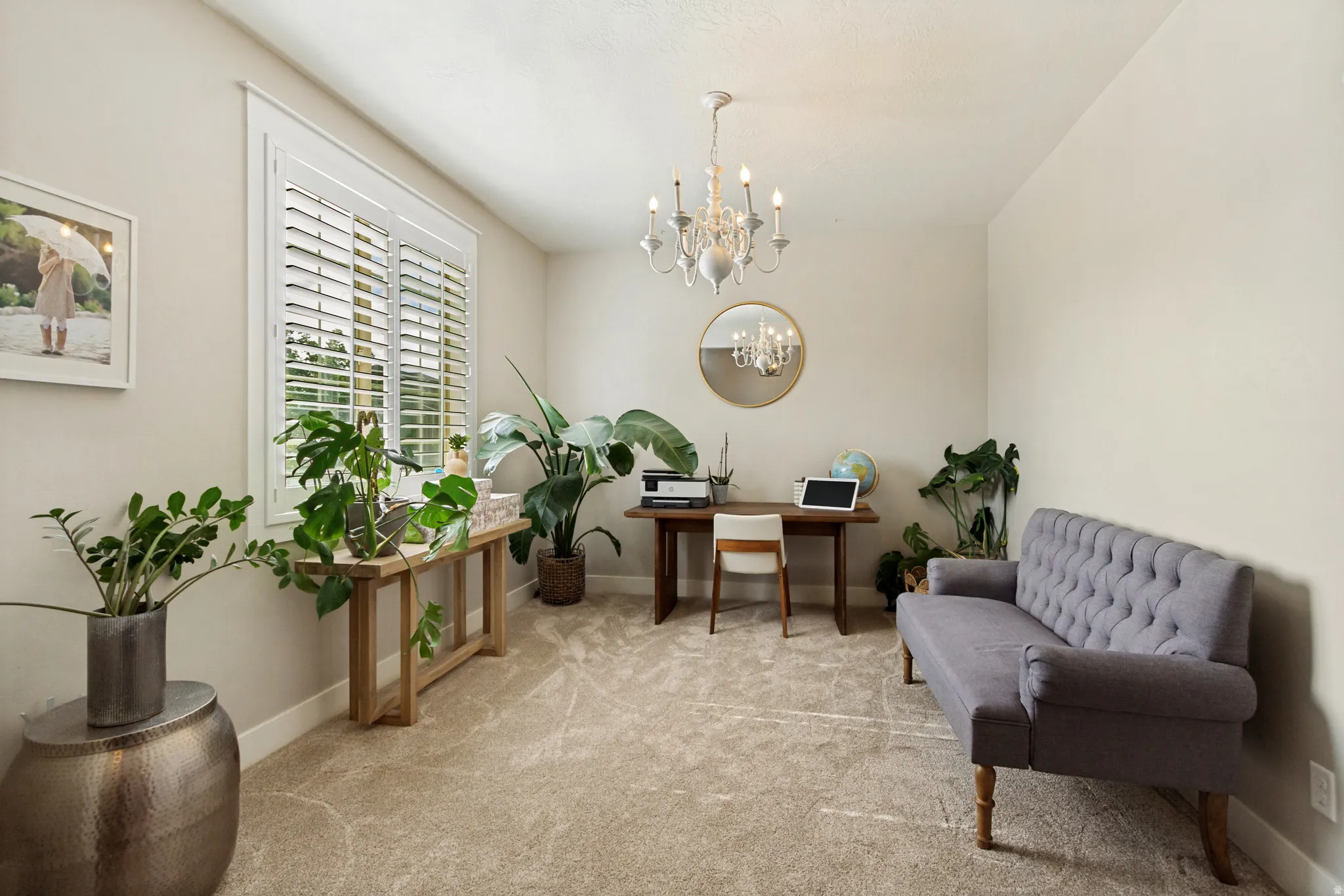 Window with plantation shutters, overhead chandelier, light neutral paint, and textured carpet flooring