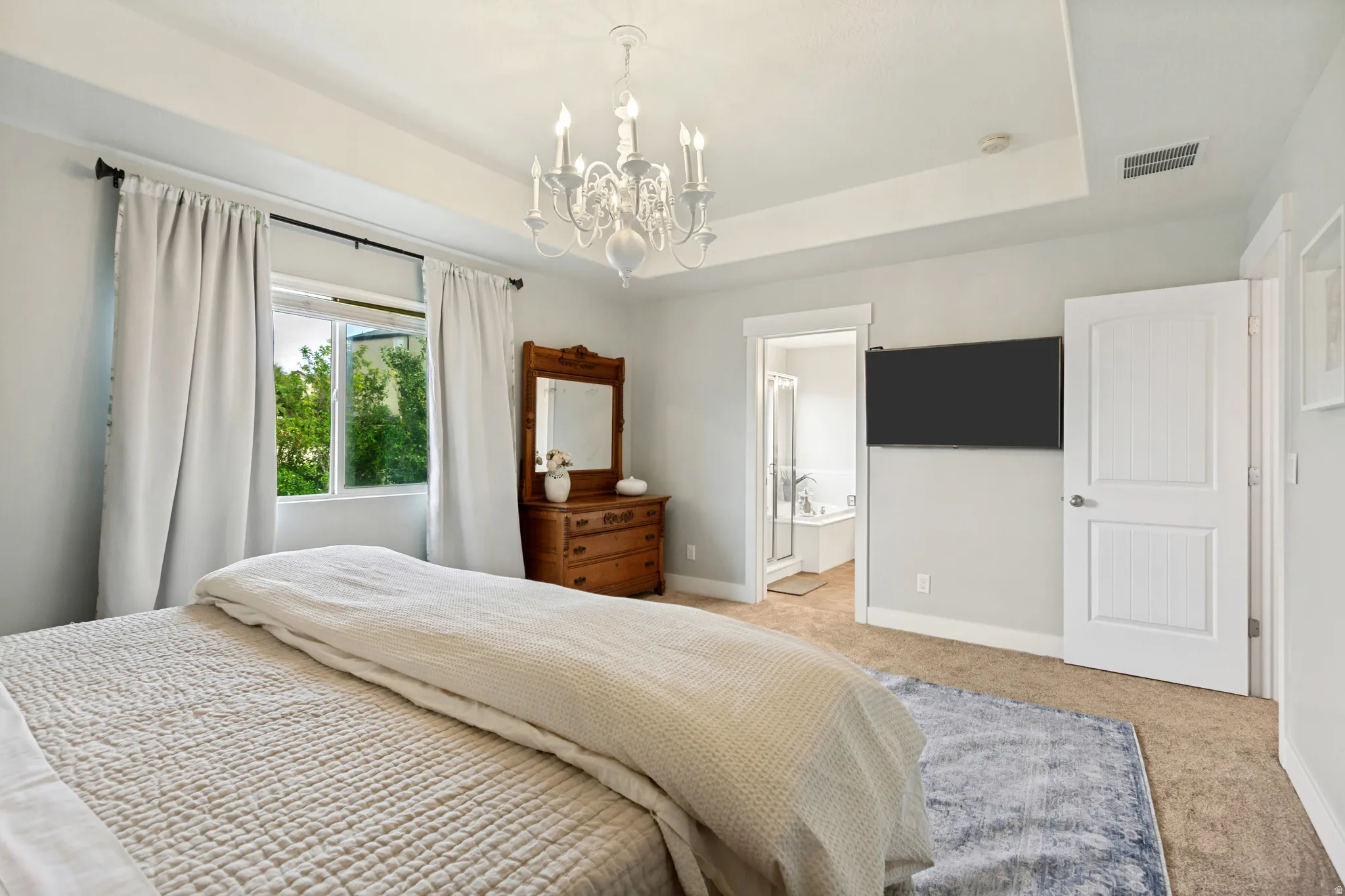 Tray ceiling with a decorative chandelier, white paneled doors, and a window with a green outdoor scene