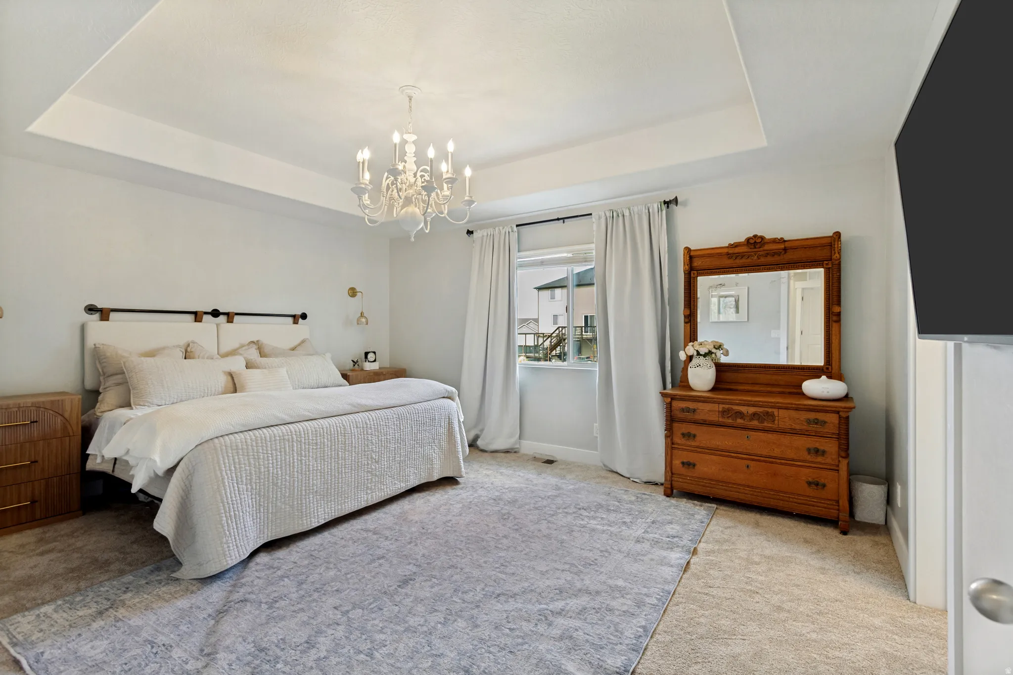 Tray ceiling with a decorative chandelier, dual sconce lighting, and carpeted flooring