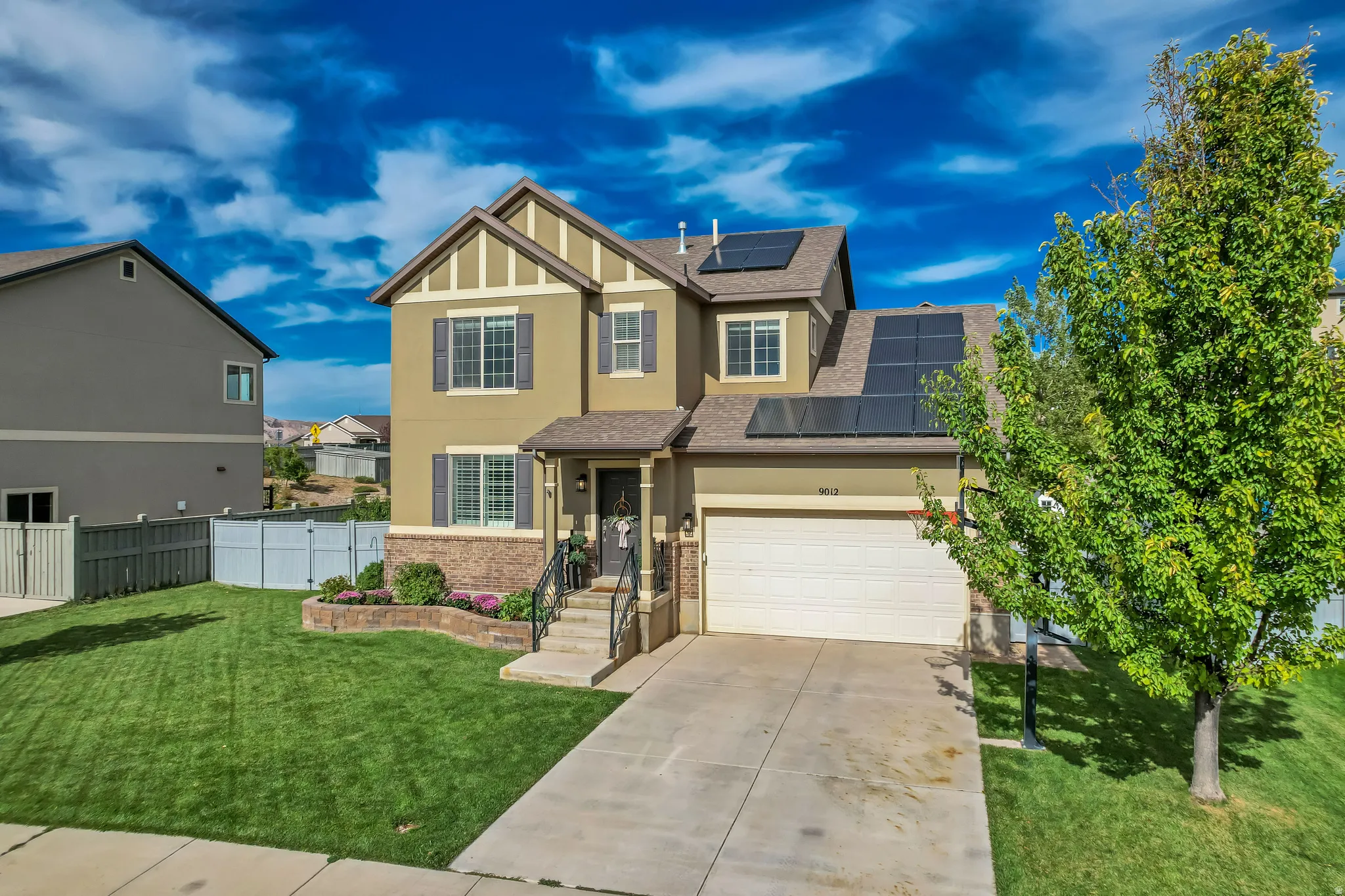 Two-story exterior with stucco and brick accents, solar panels, attached garage, and a concrete driveway